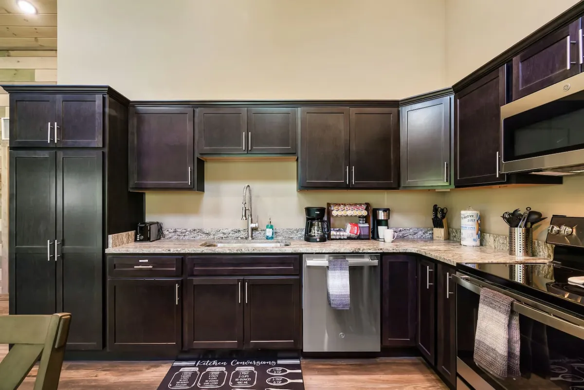 The photo highlights a stylish, modern kitchen with dark wooden cabinets, granite countertop, and stainless steel appliances. The layout suggests an open, functional cooking space ideal for meal prep or casual conversation while cooking.