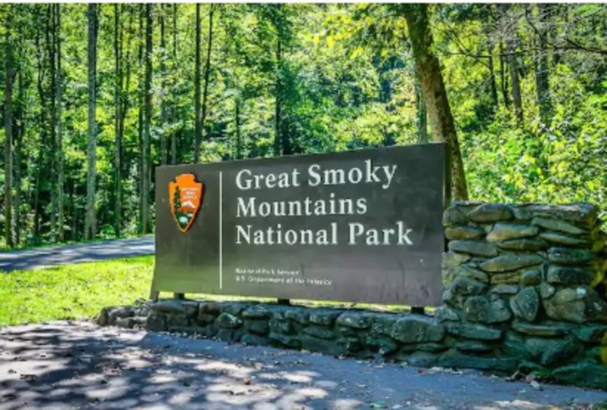 A park entrance sign surrounded by lush trees and a stone wall, hinting at nearby hiking trails and opportunities for wildlife observation.