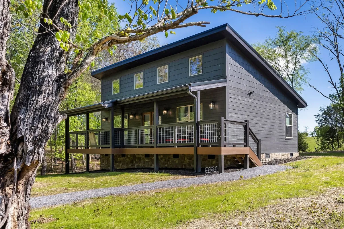 The image showcases the cabin's inviting front porch with comfortable seating, framed by large windows that let in natural light. Surrounded by lush woods, the scene exudes tranquility and promises stunning sunset views. The overall atmosphere is warm and serene, inviting guests to relax and unwind in nature.