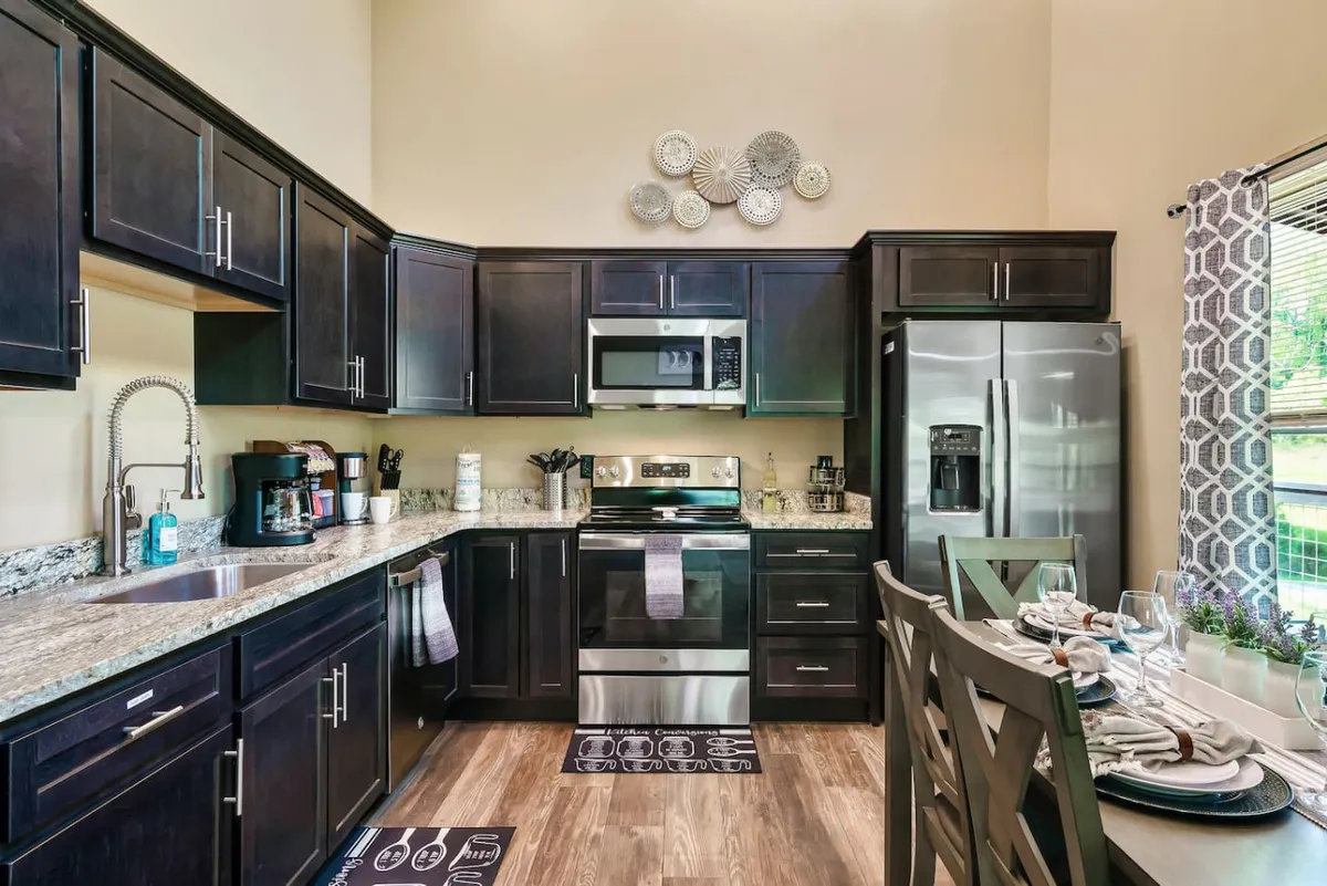 This image showcases a modern kitchen with dark cabinetry, granite countertops, stainless steel appliances, and decorative wall art. The adjacent dining table is set, creating a seamless, inviting atmosphere for both cooking and gathering. The scene exudes warmth and togetherness, highlighting the potential for family meals or entertaining guests.