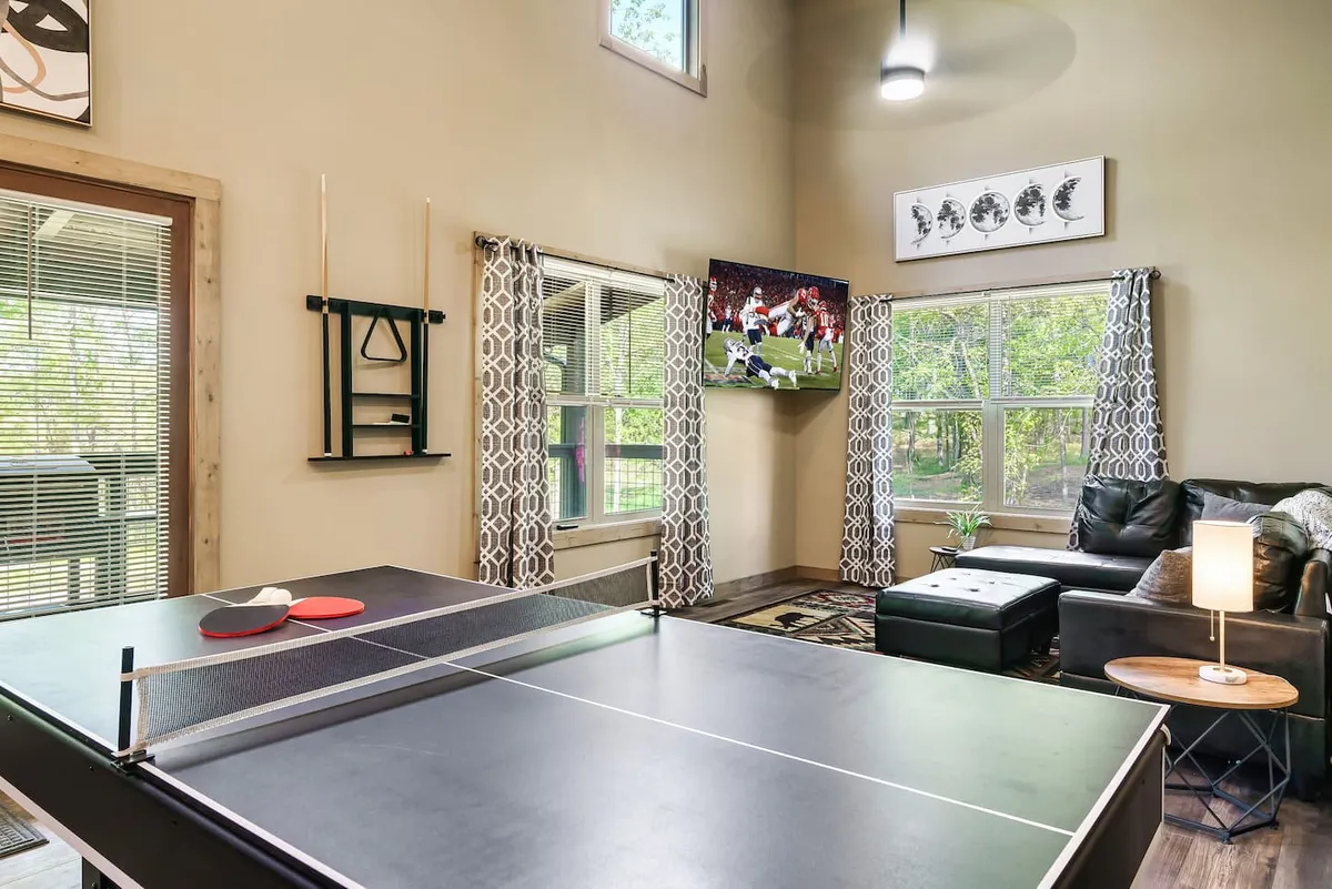 A dynamic recreation area showcasing a ping pong table, a large TV, and a sofa positioned to take in both the games and the serene views outside the big windows. The setting encourages lively interaction and relaxation.