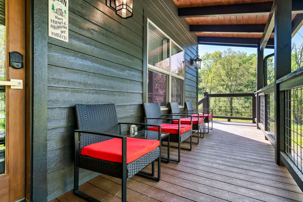 A welcoming porch area with red cushioned chairs set beside a wooden railing and lantern-style lighting. The setting overlooks a tranquil, wooded landscape, inviting relaxation and moments of wildlife observation.