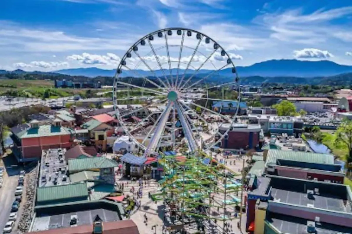 This image captures a vibrant exterior view of The Island in Pigeon Forge, featuring the iconic ferris wheel, colorful attractions, and a lively crowd of visitors. The scene radiates energy and excitement, perfectly showcasing one of the region's most popular family destinations.